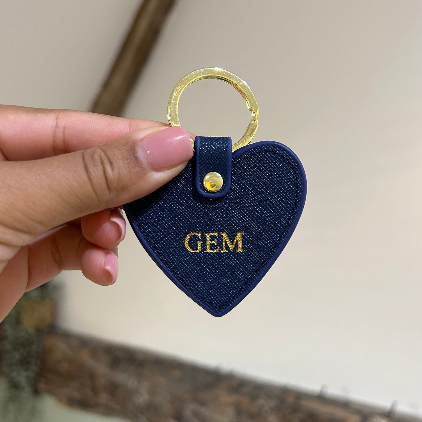 Navy blue keychain with 'GEM' text held by a hand against a neutral background