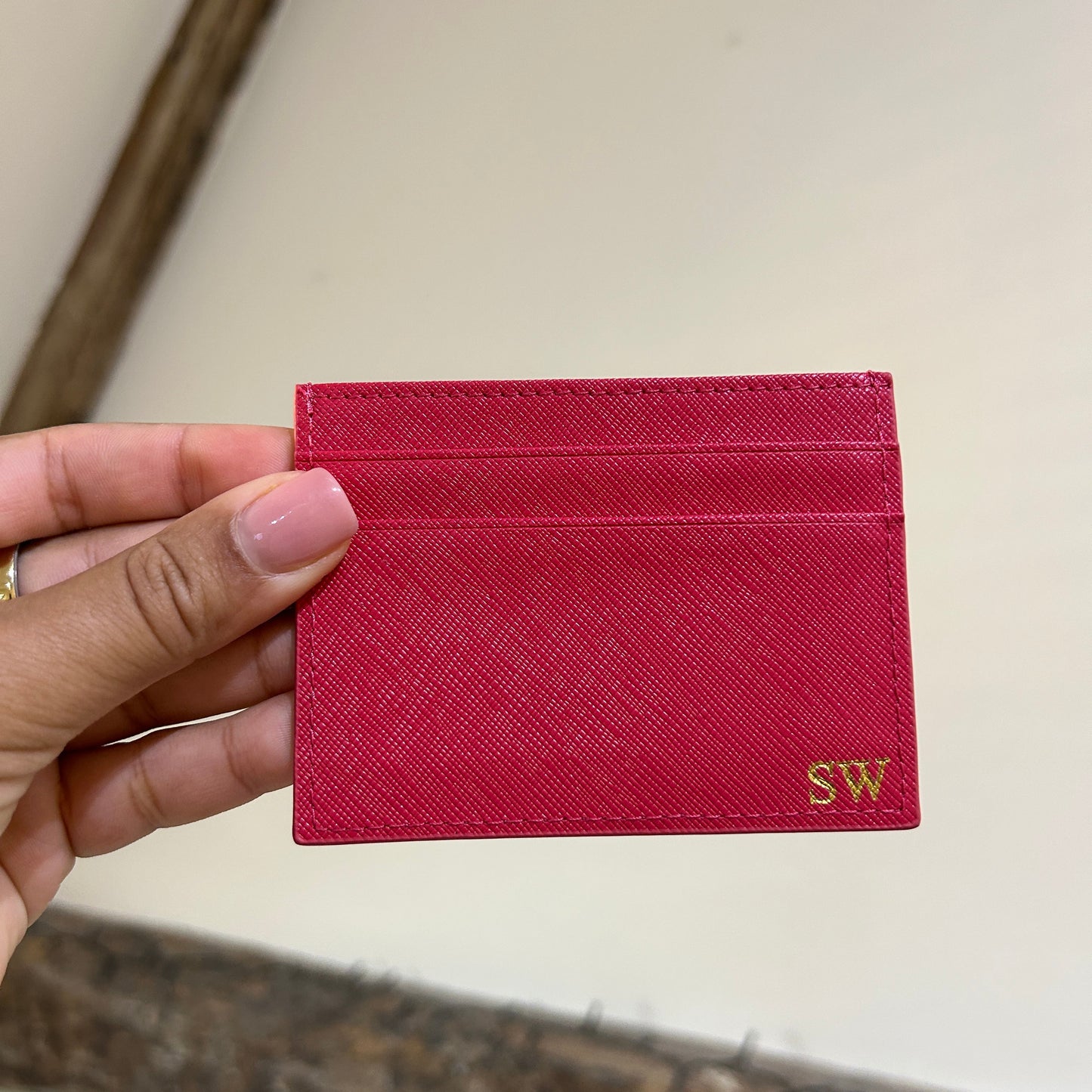 Red cardholder with gold initials held by a hand against a neutral background