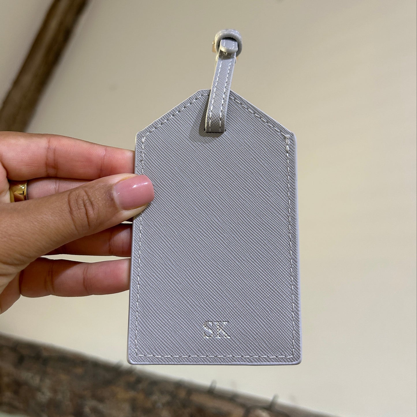 Hand holding a gray textured luggage tag against a neutral background