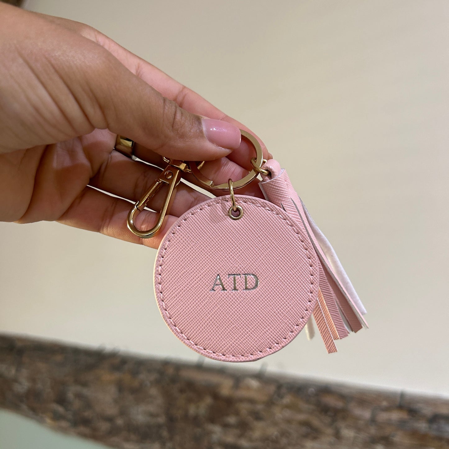 Pink keychain with circular tag held by a hand against a neutral background
