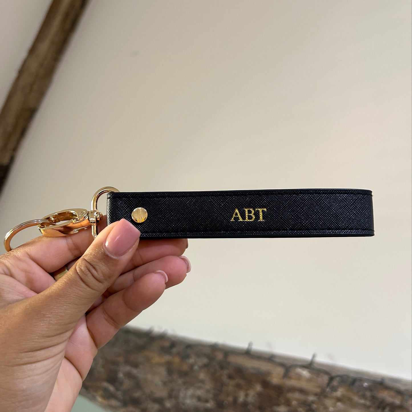 Black keychain with 'ABT' initials held by a hand against a neutral background