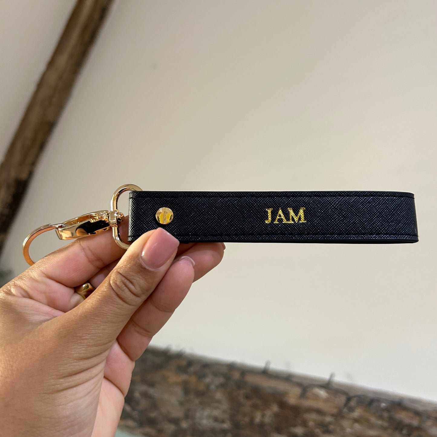 Black keychain with 'JAM' branding held by a hand against a neutral background