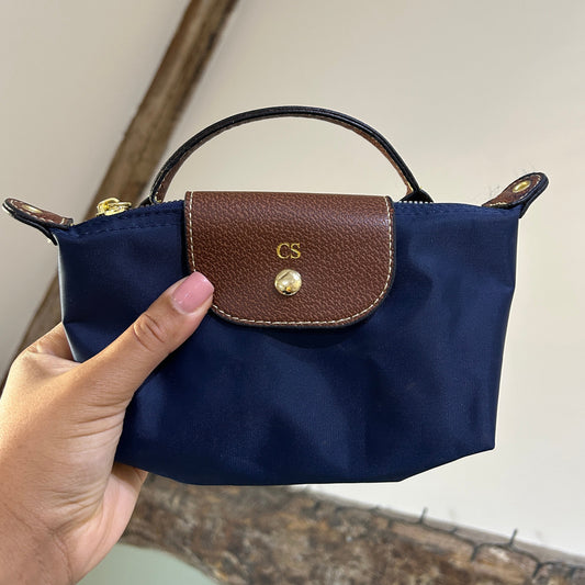 Navy blue handbag with brown leather flap held by a hand against a neutral background