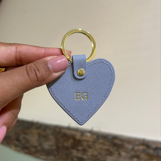 Heart-shaped blue keychain with gold ring held by a hand against a neutral background