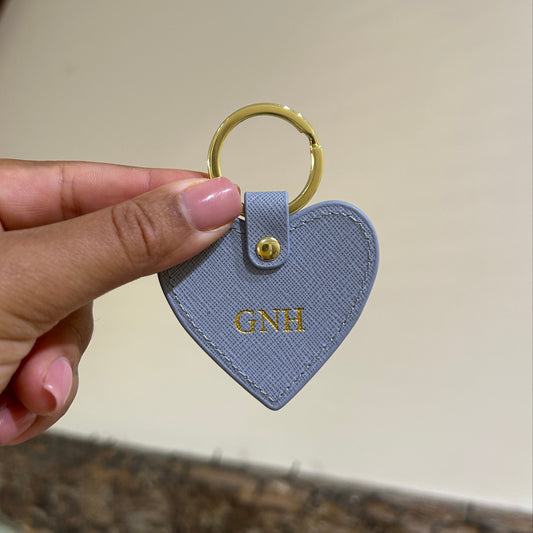 Heart-shaped keychain held by a hand against a neutral background