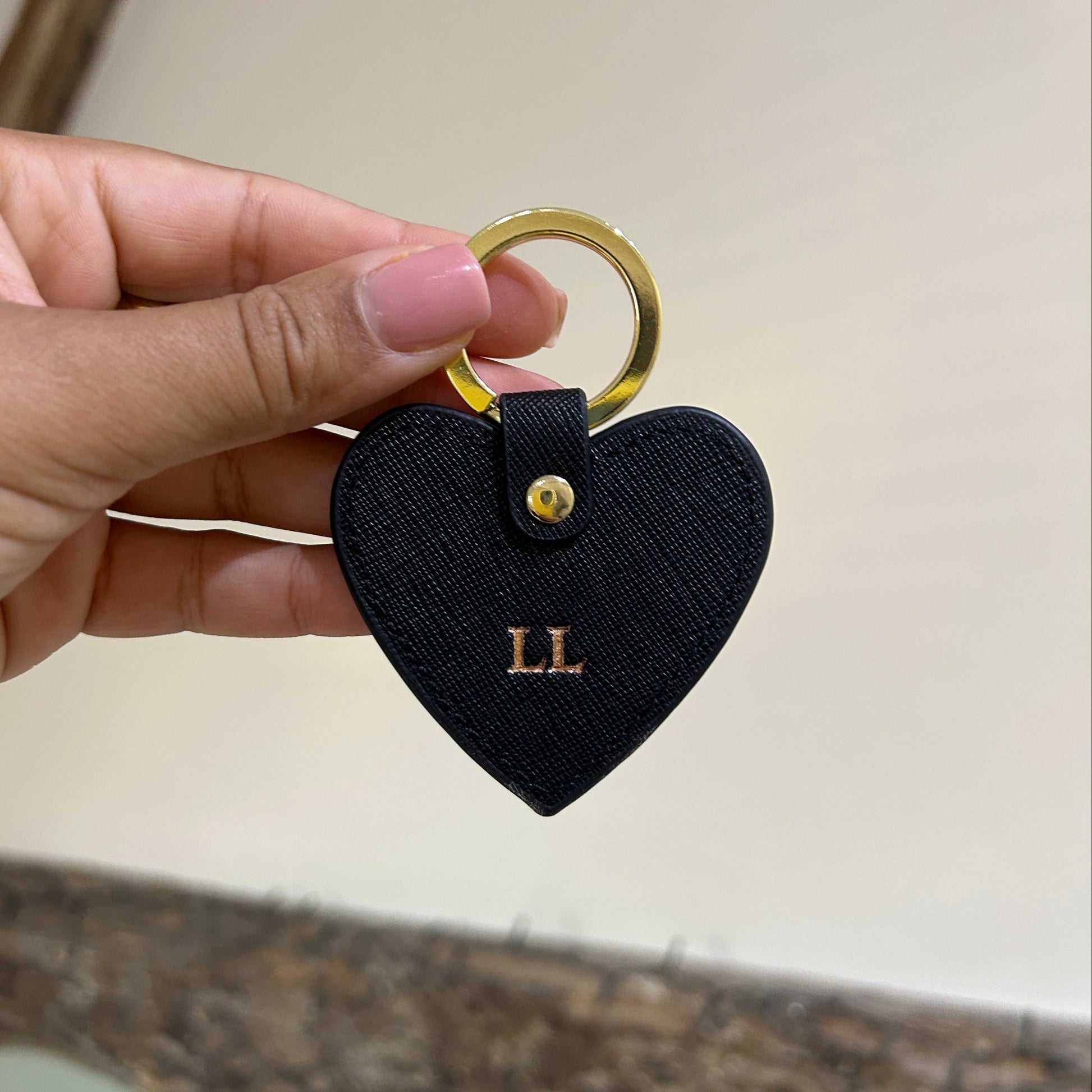 Heart-shaped keychain with gold ring held by a hand against a neutral background