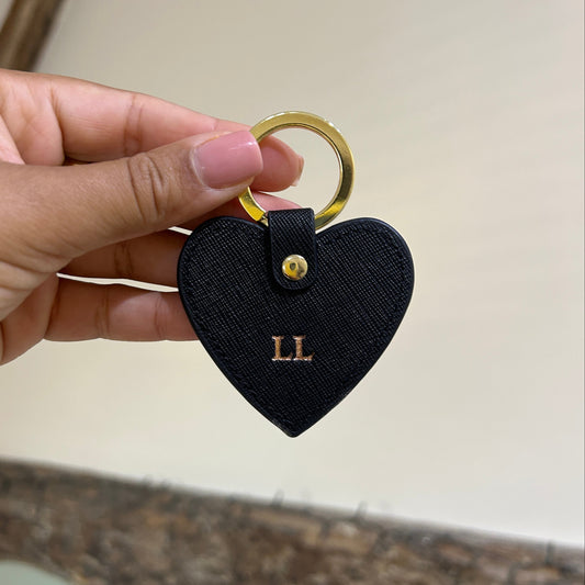 Heart-shaped keychain with gold ring held by a hand against a neutral background