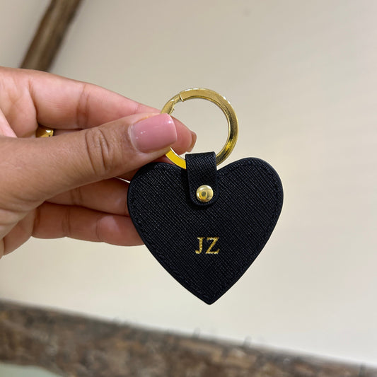 Heart-shaped black keychain with gold ring held by a hand against a neutral background