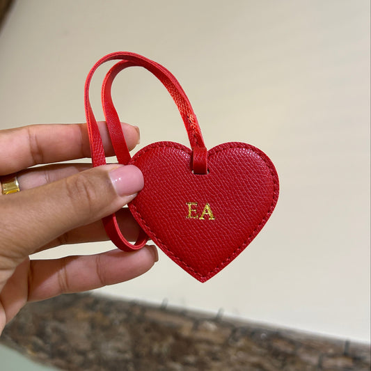 Red heart-shaped keychain held by a hand against a neutral background
