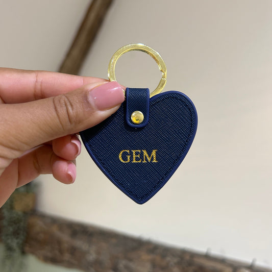 Navy blue keychain with 'GEM' text held by a hand against a neutral background