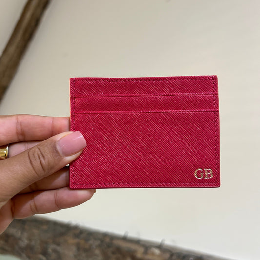 Red cardholder with gold logo held by a hand against a neutral background