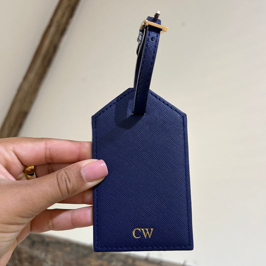 Navy blue luggage tag with initials held by a hand against a neutral background