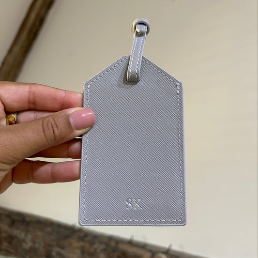 Hand holding a gray textured luggage tag against a neutral background