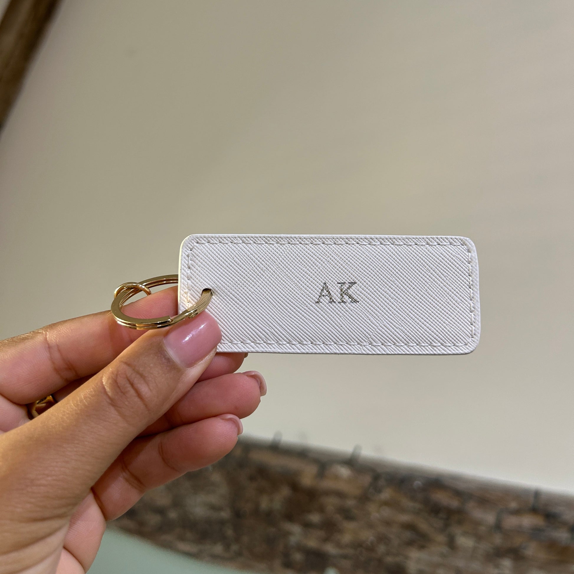 White keychain card with 'AK' initials held by a hand against a neutral background