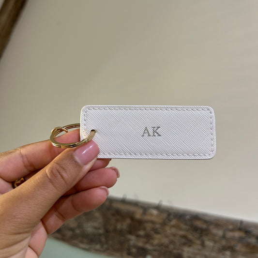 White keychain card with 'AK' initials held by a hand against a neutral background