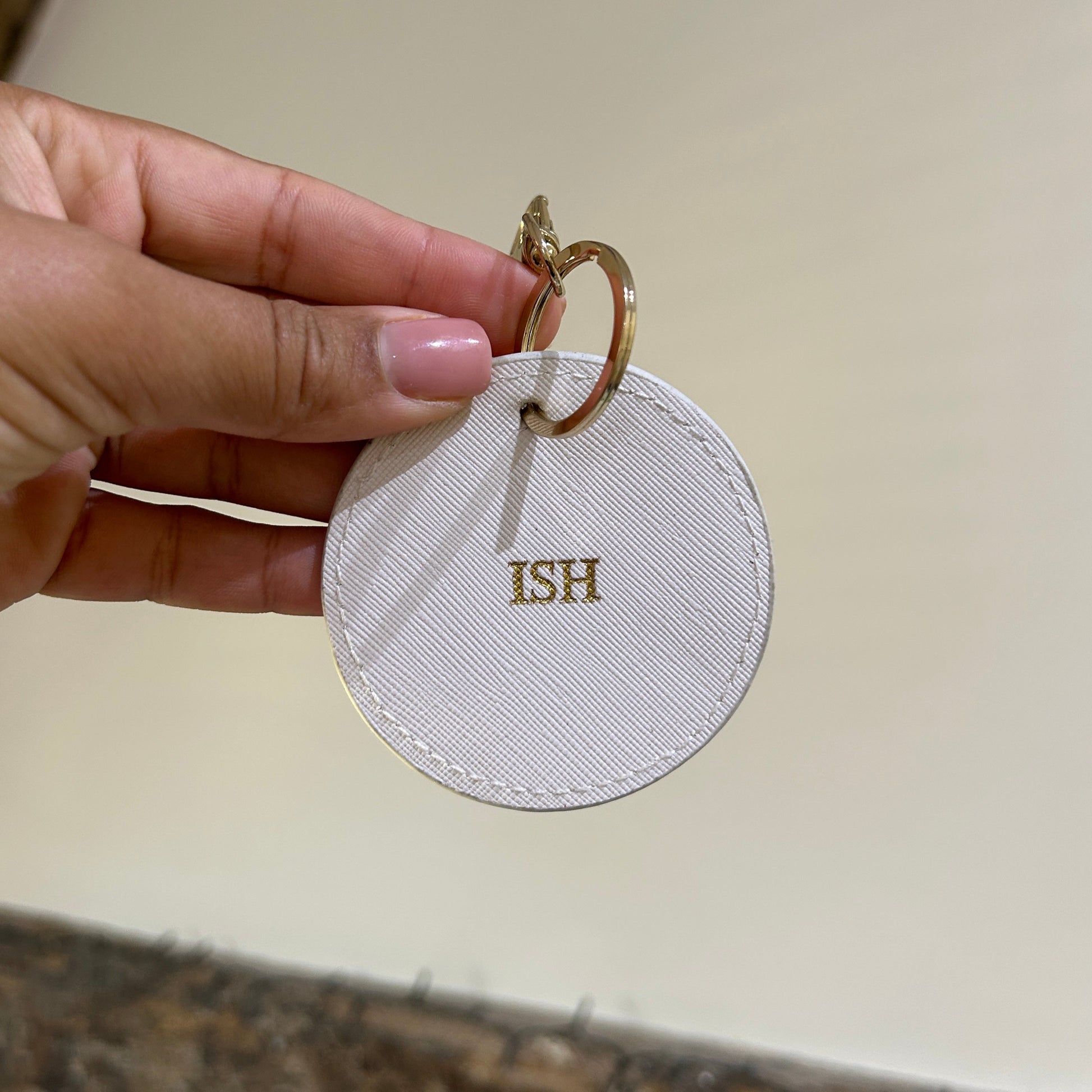 Round white keychain with 'HIS' on a beige background