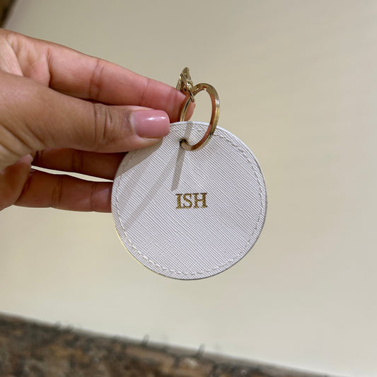 Round white keychain with 'HIS' on a beige background