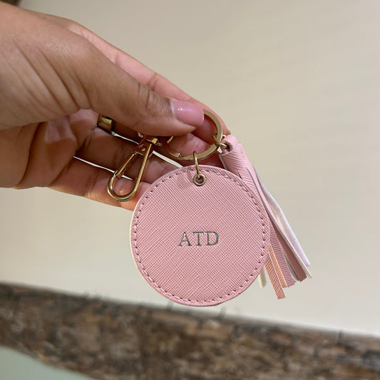 Pink keychain with circular tag held by a hand against a neutral background