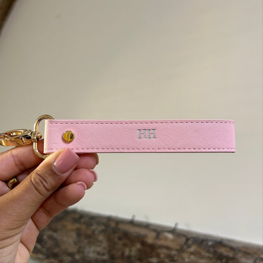 Pink leather keychain held by a hand against a neutral background