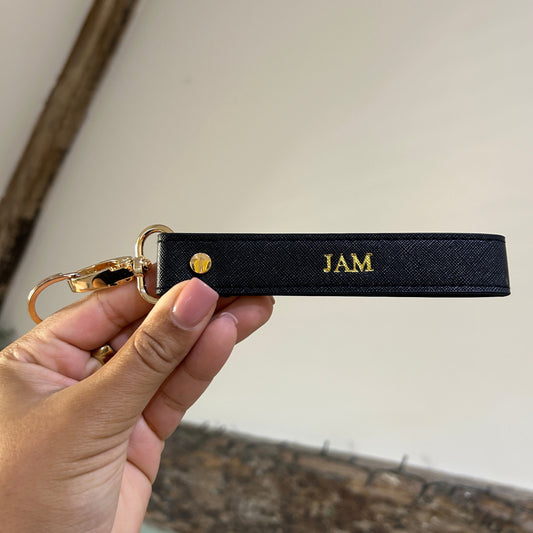 Black keychain with 'JAM' branding held by a hand against a neutral background