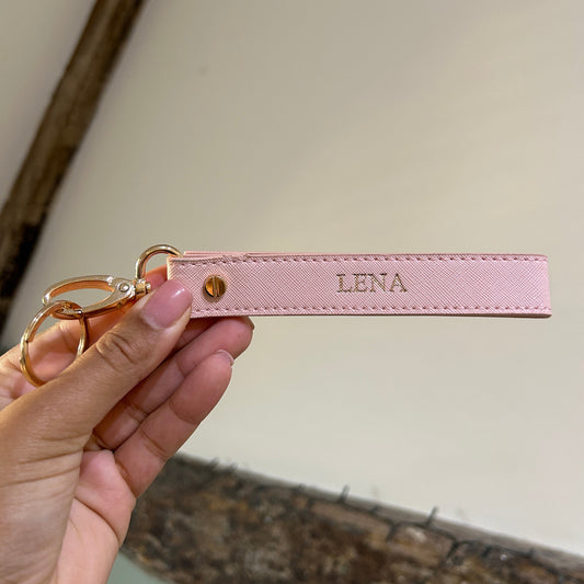 Pink keychain with 'LENA' branding held by a hand against a neutral background