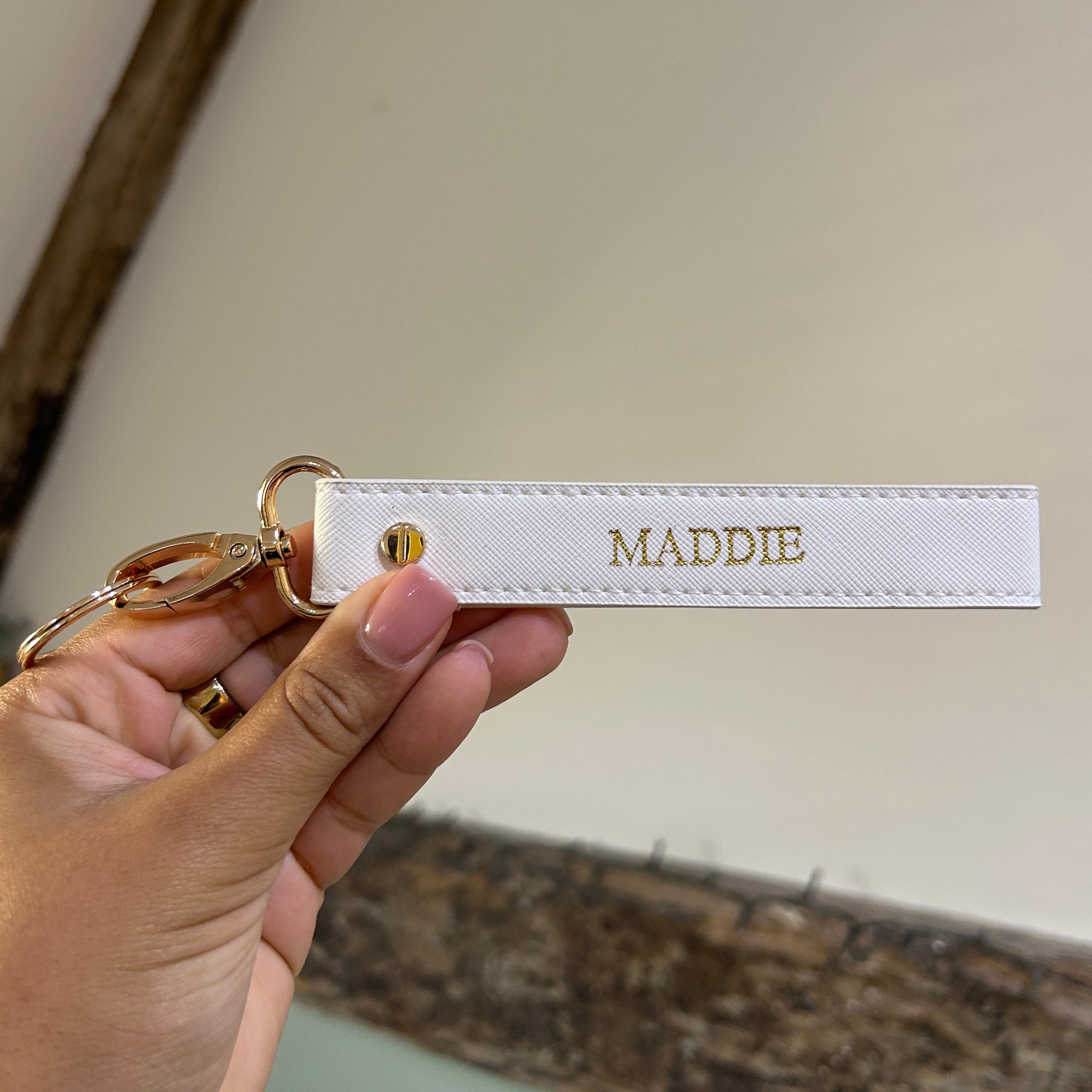 Hand holding a keychain with 'MADDIE' on a neutral background