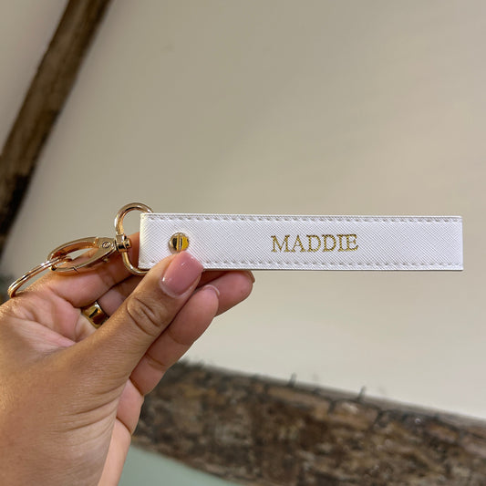 Hand holding a keychain with 'MADDIE' on a neutral background