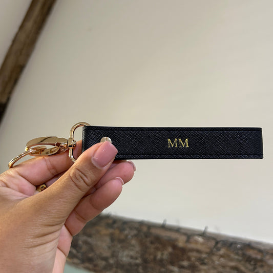Black keychain strap with gold hardware held by a hand against a neutral background