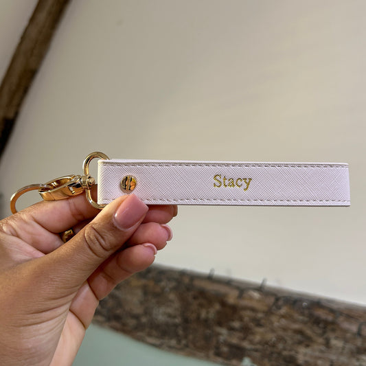 White keychain with 'Stacy' engraved, held by a hand against a neutral background