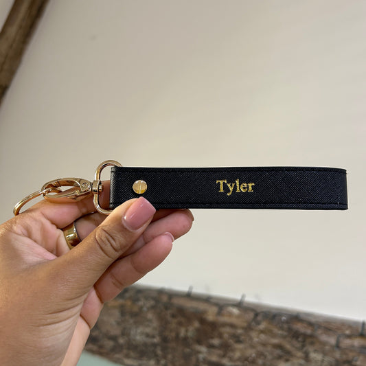 Black leather keychain with 'Tyler' engraving held by a hand against a neutral background