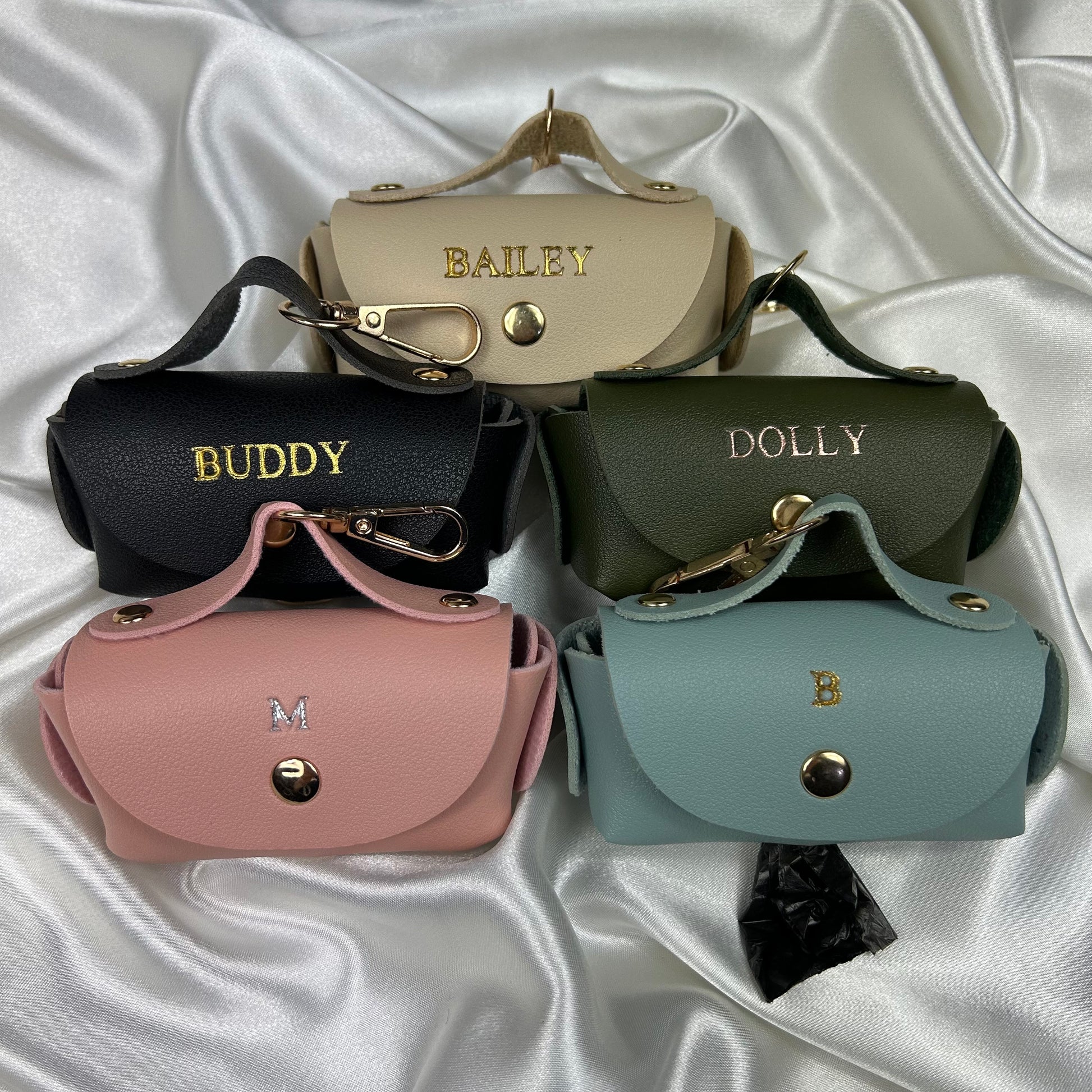personalised dog poo bag holders in colours beige, black, khaki, pink and blue. Made of vegan leather and stamped with the dogs name in gold silver and rose gold stamping to customise.